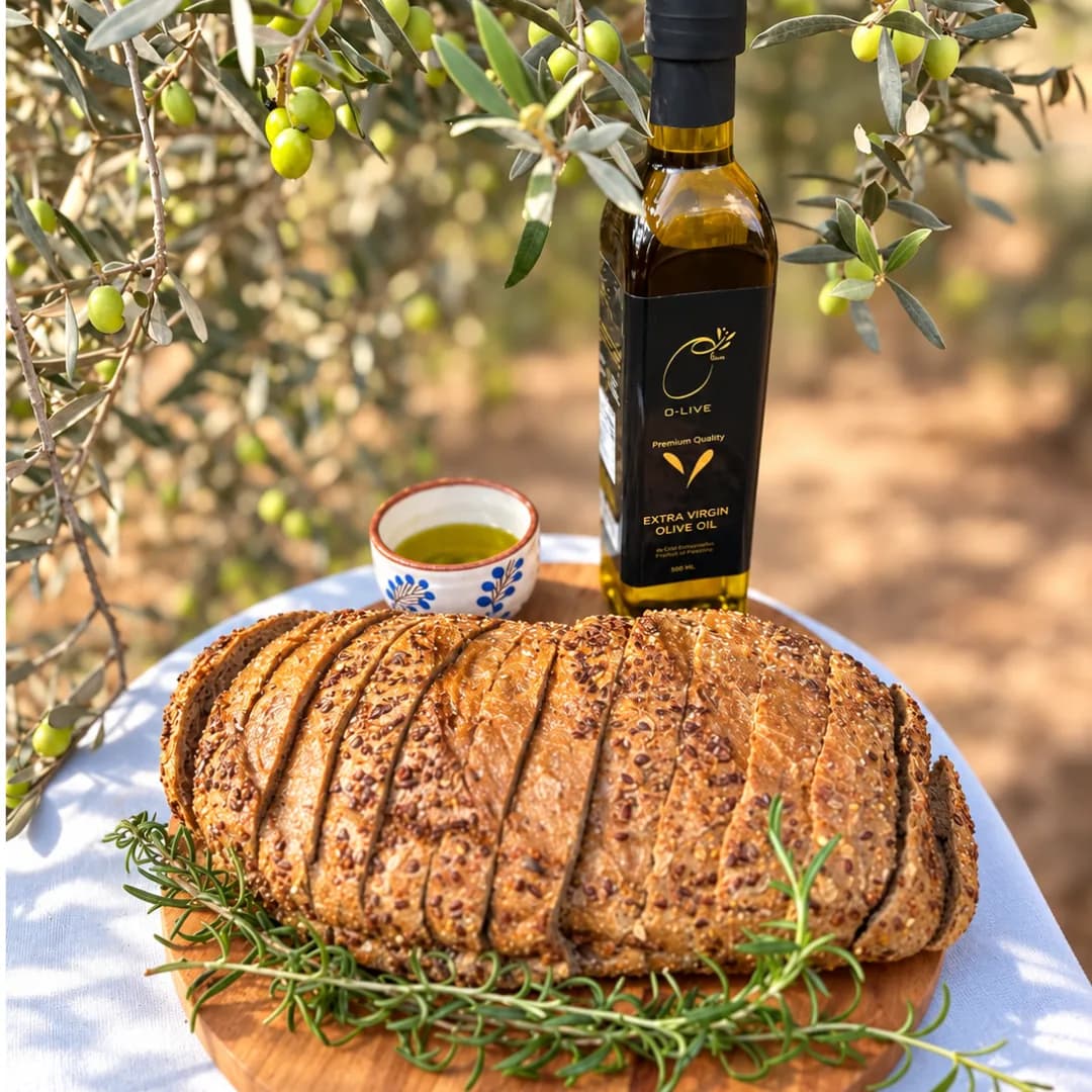 An O-Live bottle on a loaf of bread with rosemary and a cup of oil